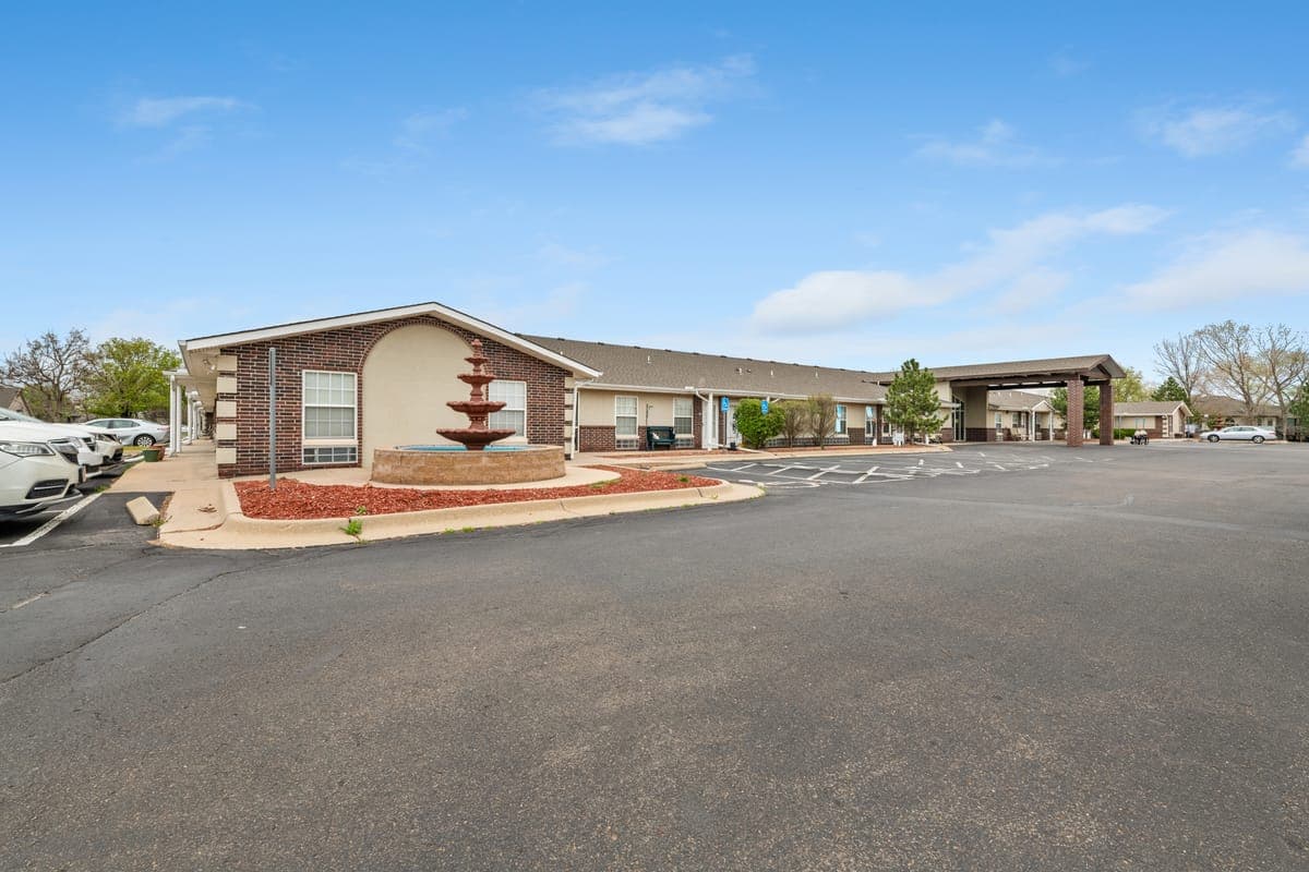 A wide view of BelVilla assisted living in Andover, Kansas, with its brick building, a tiered front fountain, and the covered main entrance.