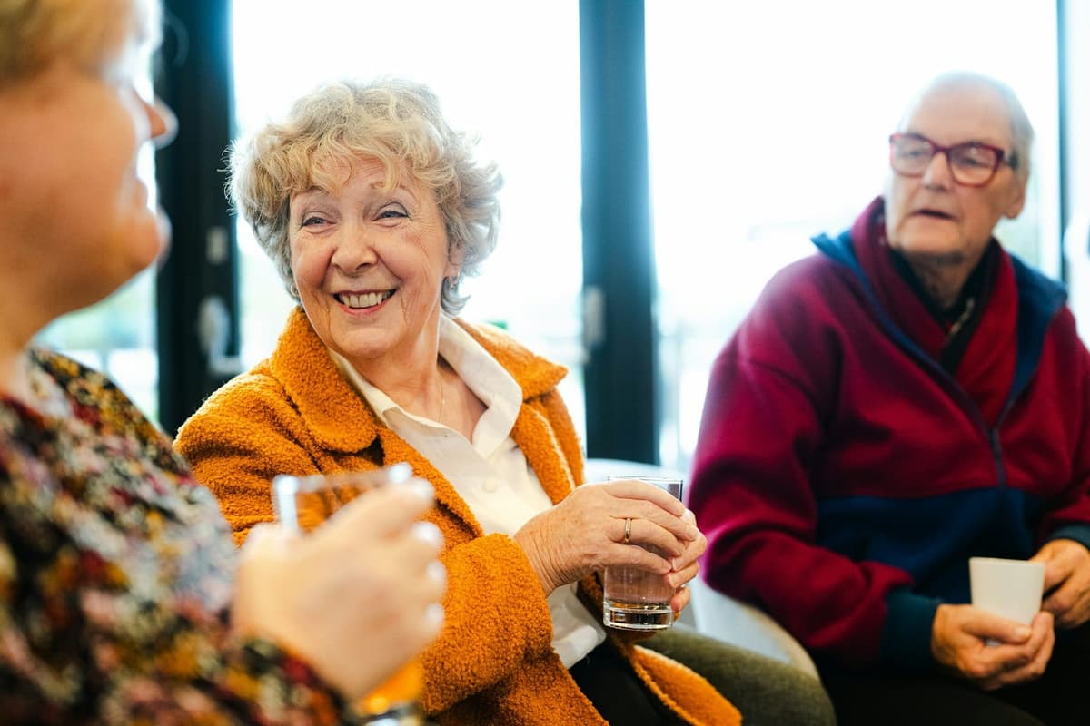 Three friends talking and laughing together over drinks.
