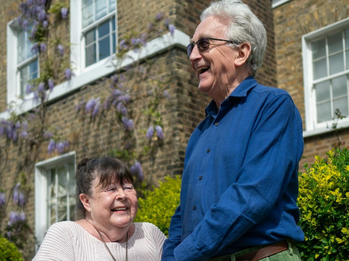 An older couple laughing together outside on a sunny day.