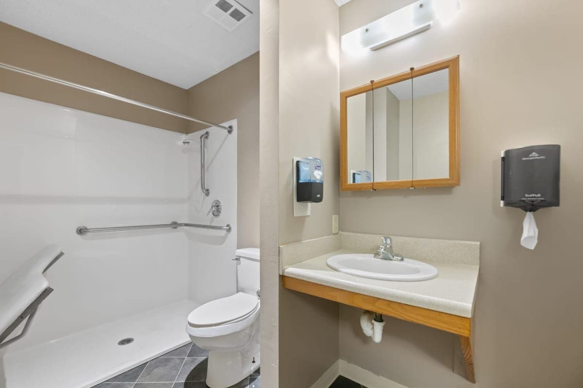 An accessible resident bathroom at BelVilla with a roll-in shower and grab bars.