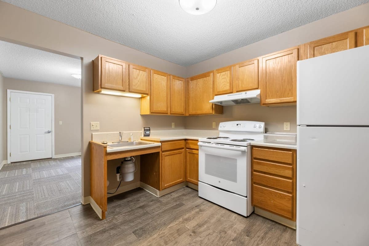A resident kitchen at BelVilla with full-size appliances, wood cabinets, and a roll-under accessible sink.